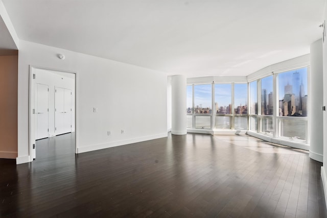 interior space with a city view, baseboards, floor to ceiling windows, and dark wood finished floors