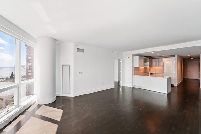 unfurnished living room with dark wood-type flooring, visible vents, recessed lighting, a sink, and baseboards