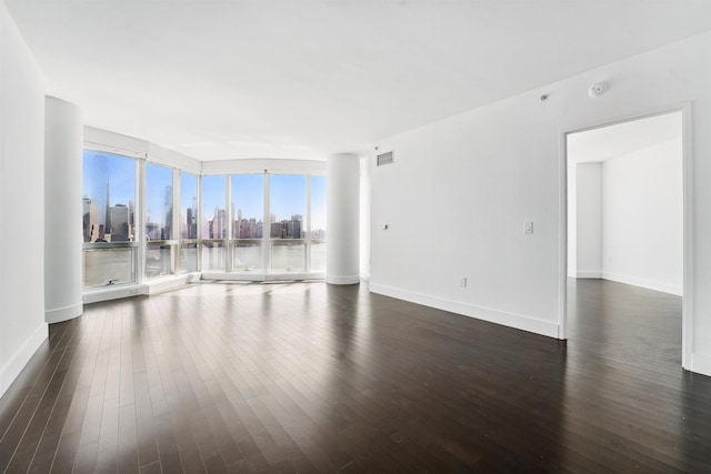 empty room with expansive windows, baseboards, a view of city, dark wood-type flooring, and visible vents