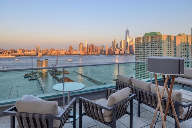 balcony at dusk featuring a water view and a view of city