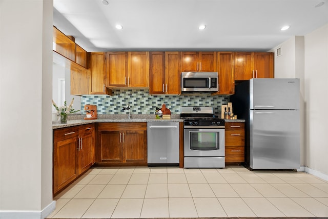 kitchen with light stone counters, brown cabinets, stainless steel appliances, backsplash, and a sink