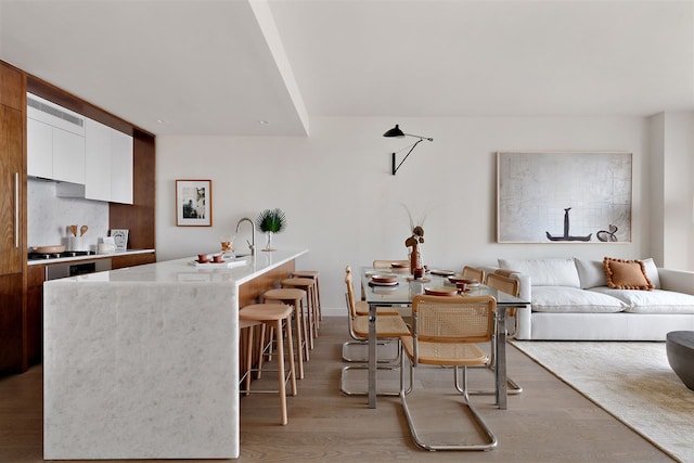 kitchen featuring a breakfast bar, a center island with sink, light hardwood / wood-style flooring, and white cabinetry