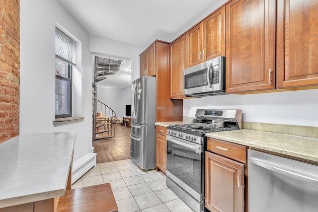 294 Barrow St Unit 6, Jersey City, NJ 07302 - kitchen with stainless steel appliances, light tile patterned floors, brown cabinets, light stone counters, and brick wall
