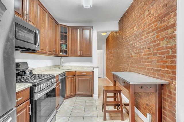 294 Barrow St Unit 6, Jersey City, NJ 07302 - kitchen featuring appliances with stainless steel finishes, brown cabinetry, brick wall, glass insert cabinets, and light tile patterned floors