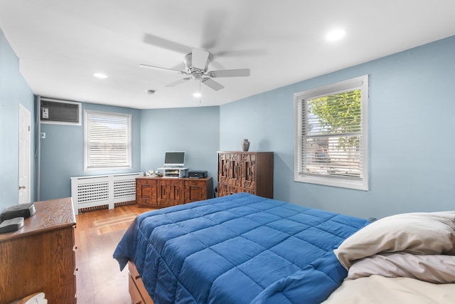 bedroom with wood finished floors, ceiling fan, radiator heating unit, recessed lighting, and a wall unit AC