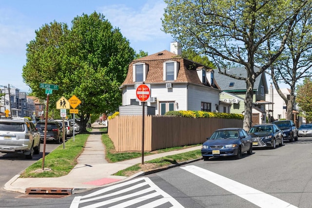 exterior space with a shingled roof, fence, mansard roof, and a chimney