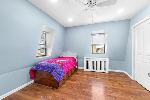 bedroom with baseboards, radiator, wood finished floors, and multiple windows