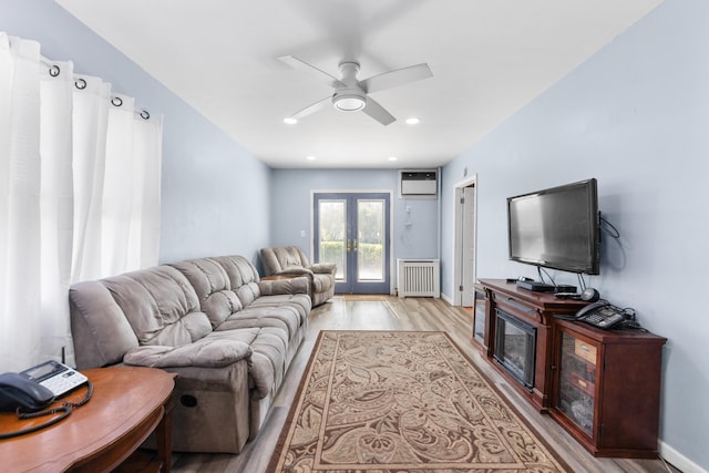 living room with ceiling fan, a wall mounted air conditioner, french doors, light wood-style flooring, and radiator