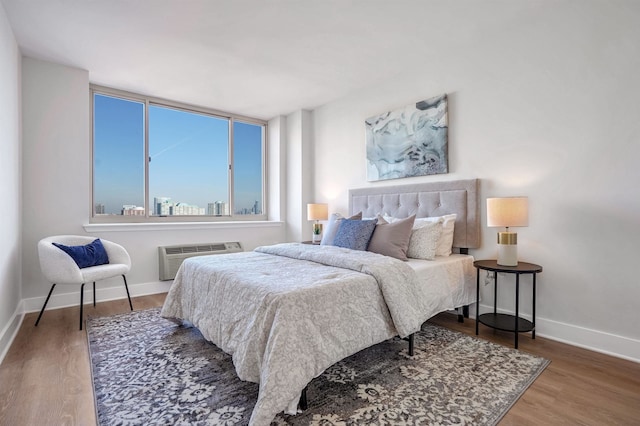 bedroom with baseboards, a wall unit AC, and wood finished floors