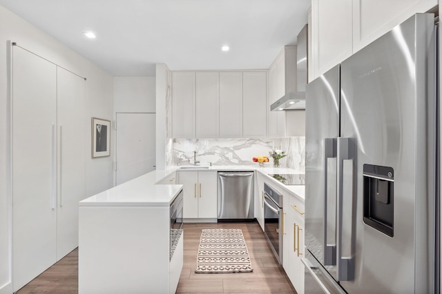 kitchen with stainless steel appliances, wall chimney exhaust hood, white cabinets, and sink