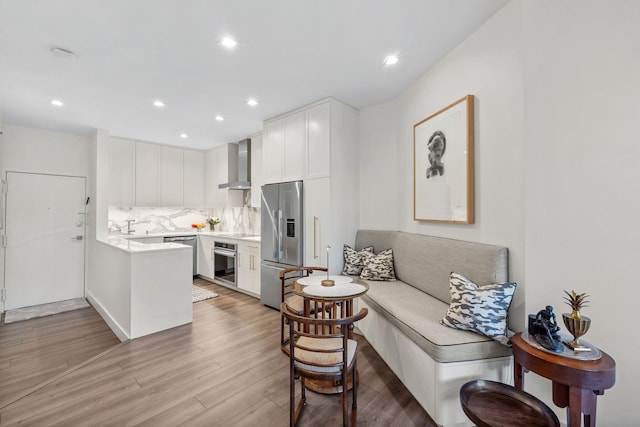 kitchen featuring light wood-style flooring, appliances with stainless steel finishes, white cabinetry, wall chimney range hood, and a peninsula