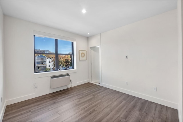 spare room featuring a wall mounted AC, wood finished floors, and baseboards