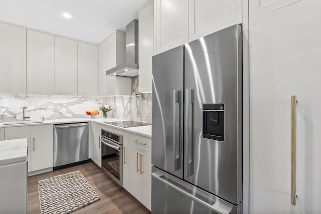 kitchen with a sink, white cabinetry, light countertops, appliances with stainless steel finishes, and wall chimney exhaust hood