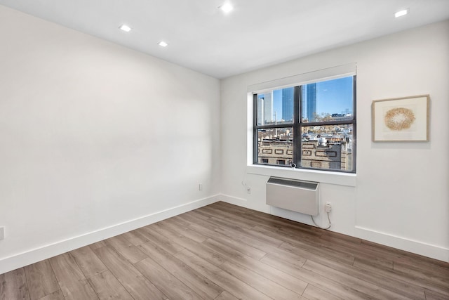 spare room with recessed lighting, a wall unit AC, wood finished floors, and baseboards