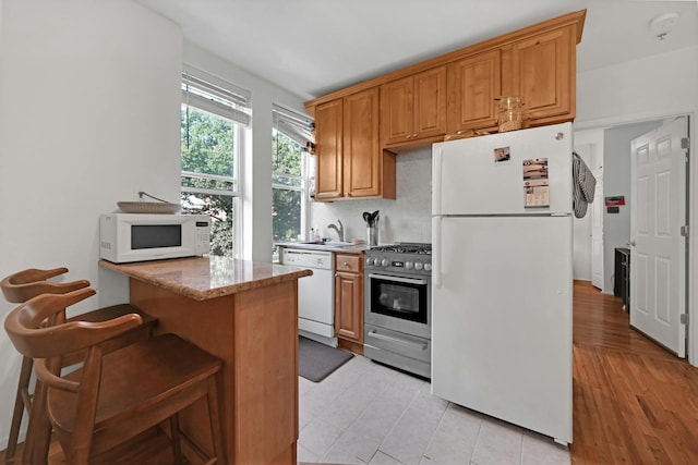 734 Adams St Unit 4B, Hoboken, NJ 07030 - kitchen featuring white appliances, a breakfast bar area, light stone counters, backsplash, and light tile patterned flooring