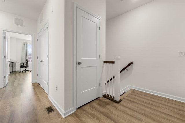 corridor with an upstairs landing, light wood-style floors, and baseboards