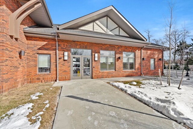 snow covered property entrance with french doors and brick siding