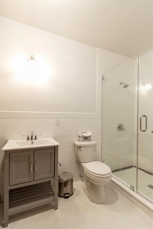 bathroom with tile patterned flooring, vanity, a shower with shower door, toilet, and tile walls