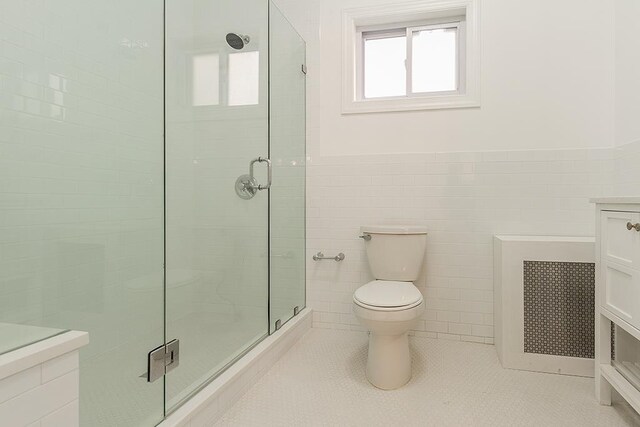 bathroom with radiator, tile walls, a shower with door, vanity, and toilet