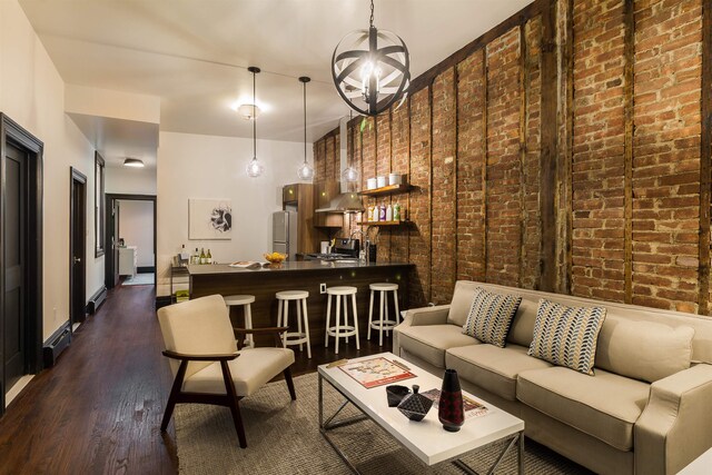 living room featuring dark wood-type flooring, brick wall, and a notable chandelier