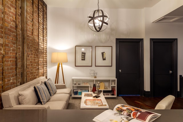 living room with dark wood-type flooring, a notable chandelier, and brick wall