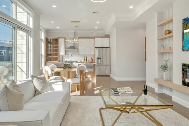 living room with built in shelves, ornamental molding, and light wood-type flooring