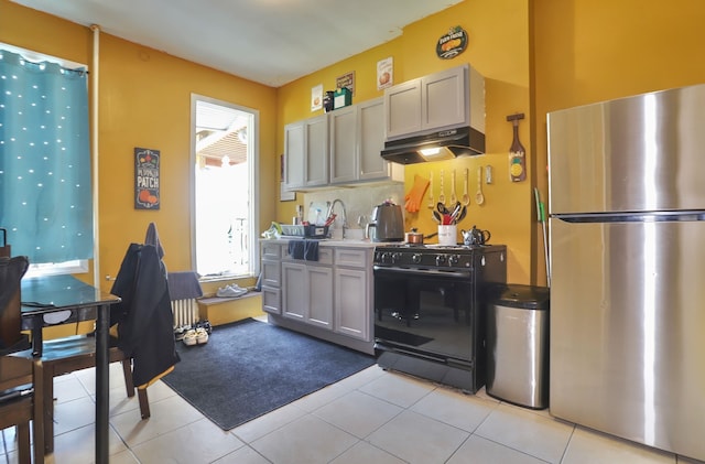 400 67th St, West New York, NJ 07093 - kitchen featuring freestanding refrigerator, black gas range oven, under cabinet range hood, light tile patterned floors, and backsplash