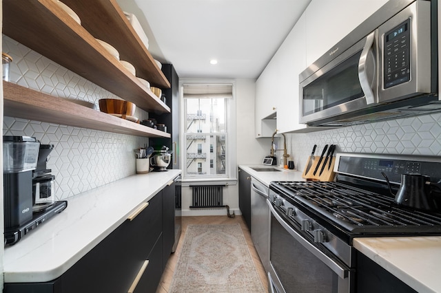 kitchen with dark cabinetry, open shelves, a sink, and stainless steel appliances