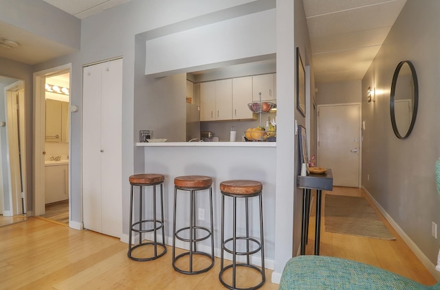 kitchen with light wood-style flooring, a kitchen bar, white cabinetry, and baseboards