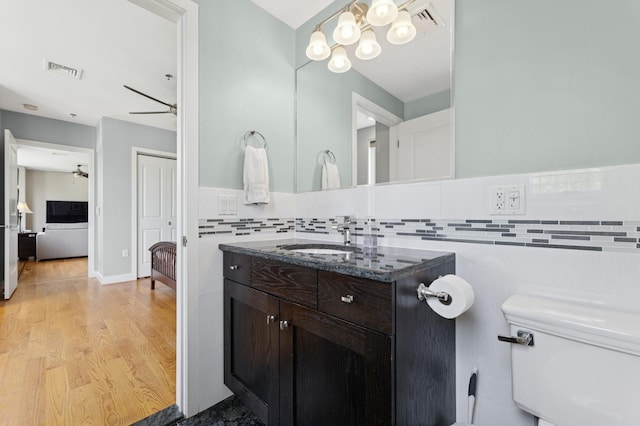bathroom featuring toilet, vanity, wood finished floors, decorative backsplash, and a ceiling fan
