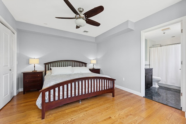 bedroom featuring wood finished floors, baseboards, ensuite bathroom, and a closet