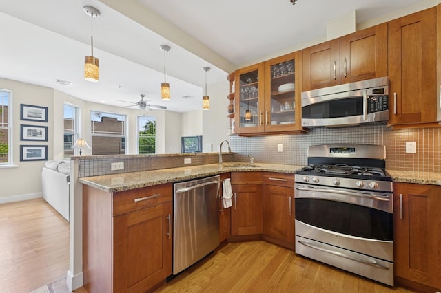 kitchen featuring stainless steel appliances, a peninsula, brown cabinetry, light wood-style floors, and tasteful backsplash