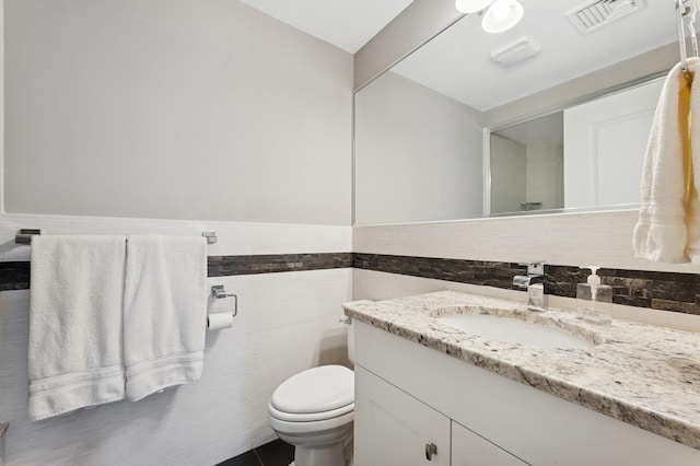 bathroom with toilet, tile walls, vanity, and wainscoting