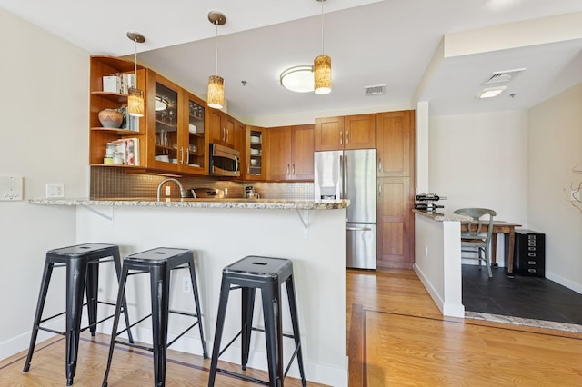 kitchen with stainless steel appliances, a breakfast bar, brown cabinetry, a peninsula, and glass insert cabinets