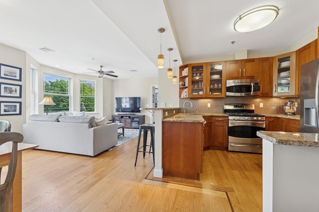 kitchen with stainless steel appliances, brown cabinetry, a kitchen breakfast bar, a peninsula, and open floor plan
