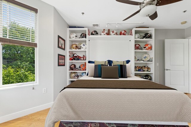 bedroom featuring multiple windows, baseboards, light wood-style flooring, and track lighting