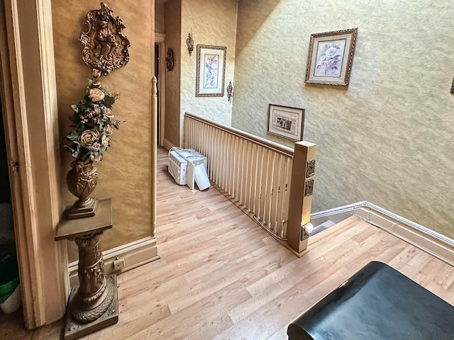 hall featuring baseboards, wood finished floors, and an upstairs landing