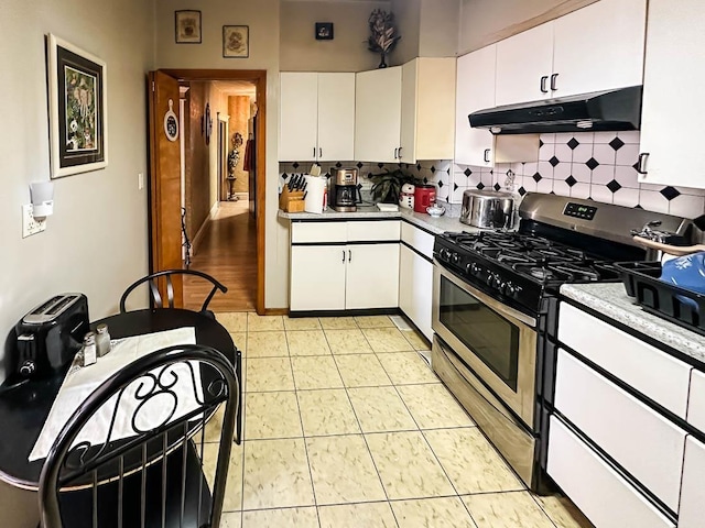 kitchen with stainless steel gas range, under cabinet range hood, white cabinets, and backsplash