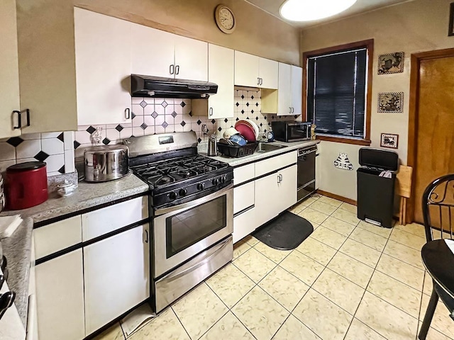 kitchen with light tile patterned floors, under cabinet range hood, stainless steel appliances, white cabinetry, and decorative backsplash