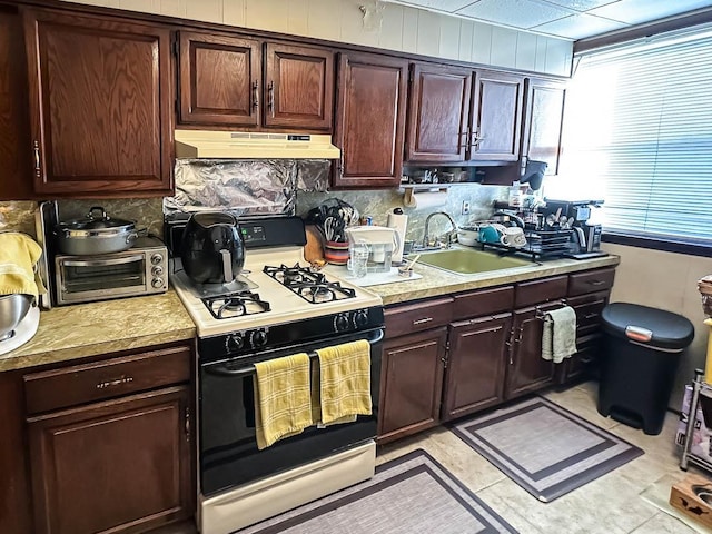 kitchen featuring a toaster, under cabinet range hood, a sink, light countertops, and gas range