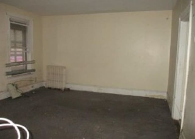 carpeted spare room featuring baseboards and radiator