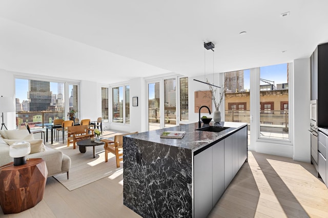 kitchen featuring sink, decorative light fixtures, light wood-type flooring, dark stone counters, and a large island