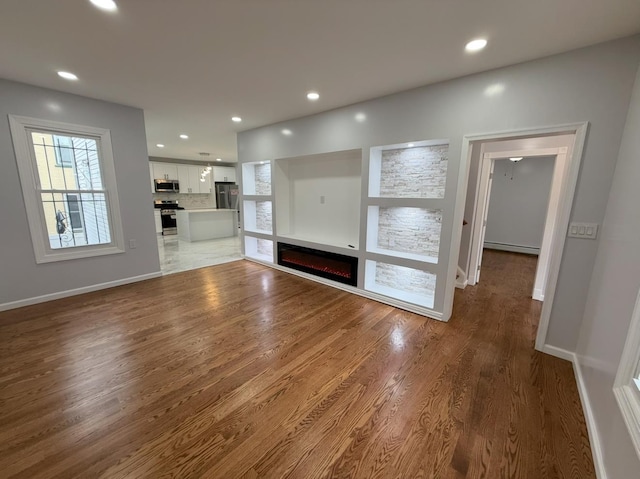 187 Lembeck Ave, Jersey City, NJ 07305 - unfurnished living room with a baseboard radiator, wood finished floors, recessed lighting, and a glass covered fireplace
