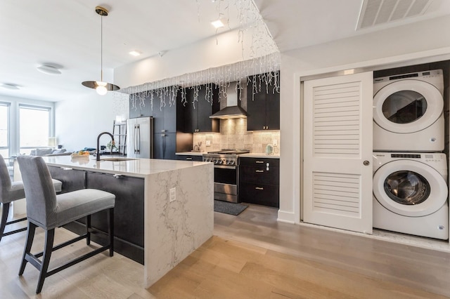 202 Merseles St Unit 504, Jersey City, NJ 07302 - kitchen featuring appliances with stainless steel finishes, wall chimney exhaust hood, stacked washer and clothes dryer, dark cabinetry, and backsplash