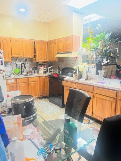 kitchen featuring tasteful backsplash, light tile patterned floors, a drop ceiling, sink, and black range with electric stovetop