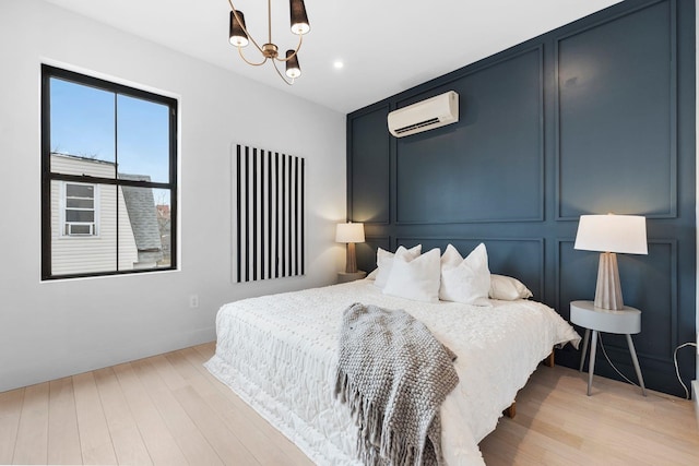 bedroom featuring a decorative wall, light wood finished floors, a notable chandelier, and a wall unit AC