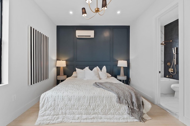 bedroom featuring baseboards, a wall mounted air conditioner, an inviting chandelier, a decorative wall, and ensuite bath