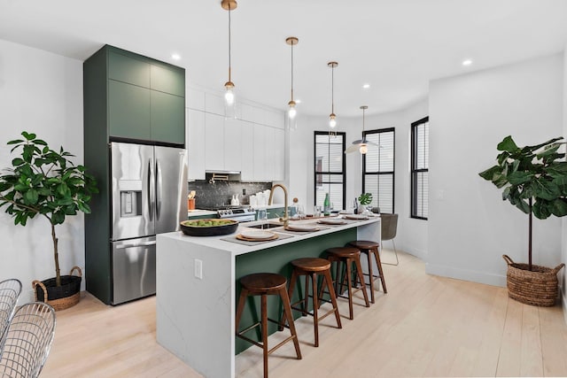 kitchen featuring light wood-type flooring, an island with sink, a sink, tasteful backsplash, and appliances with stainless steel finishes