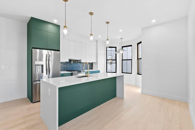 kitchen with sink, stainless steel fridge, tasteful backsplash, a center island with sink, and decorative light fixtures