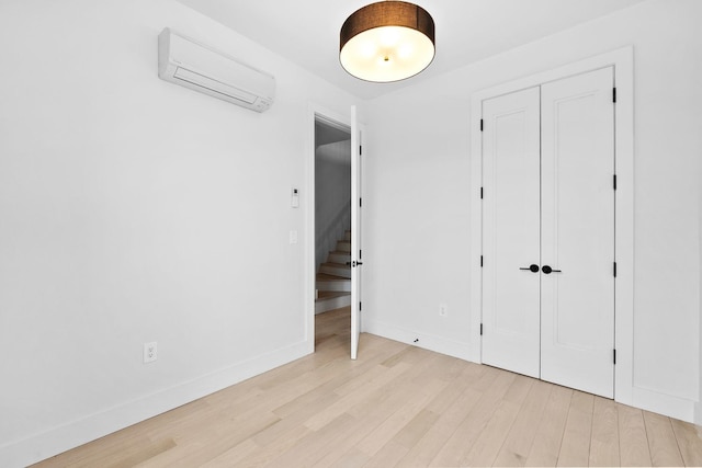 unfurnished bedroom with a closet, baseboards, light wood-style flooring, and a wall mounted AC